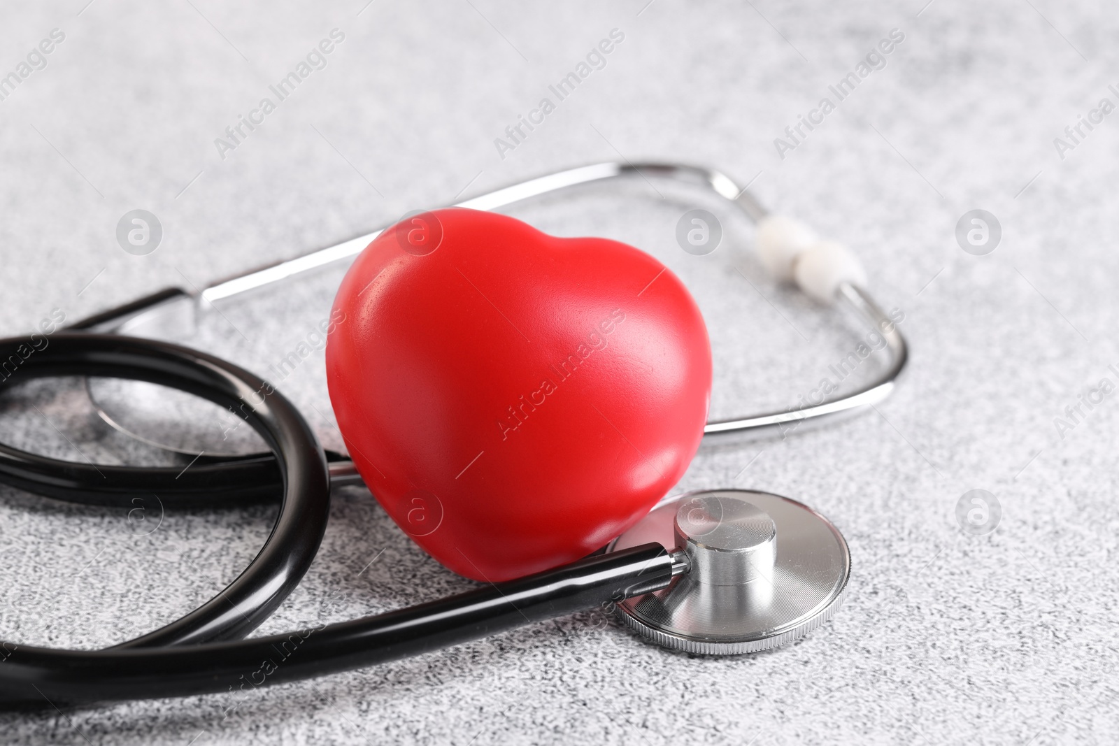 Photo of Stethoscope and red heart on grey stone table, closeup