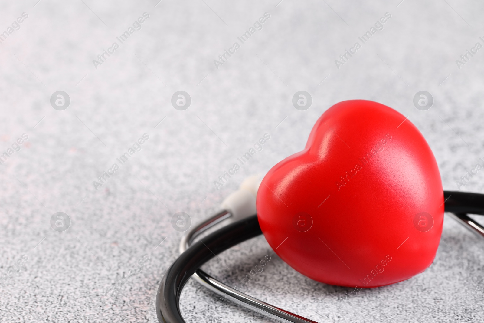 Photo of Stethoscope and red heart on grey stone table, closeup. Space for text