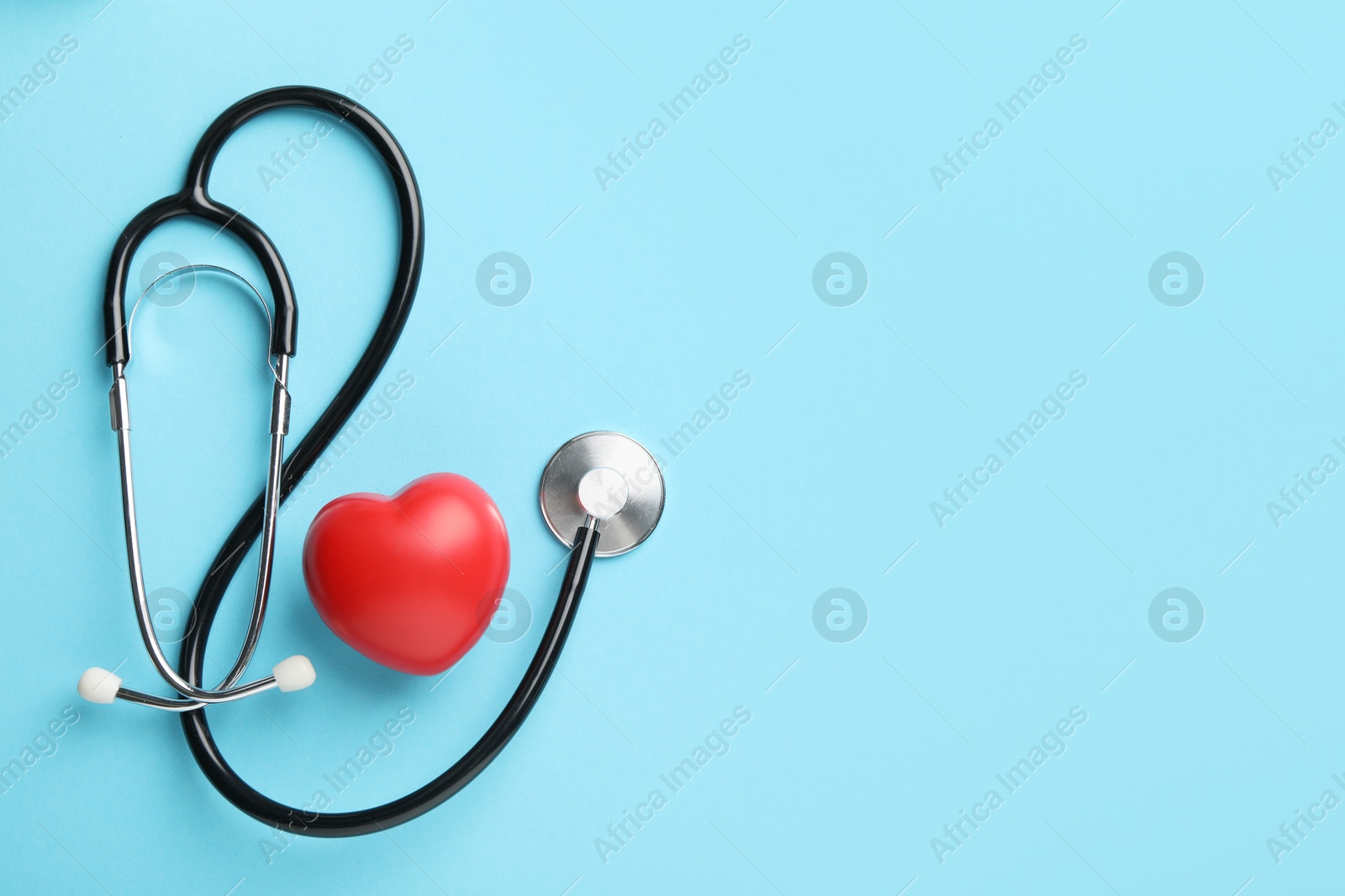 Photo of Stethoscope and red heart on light blue background, top view. Space for text