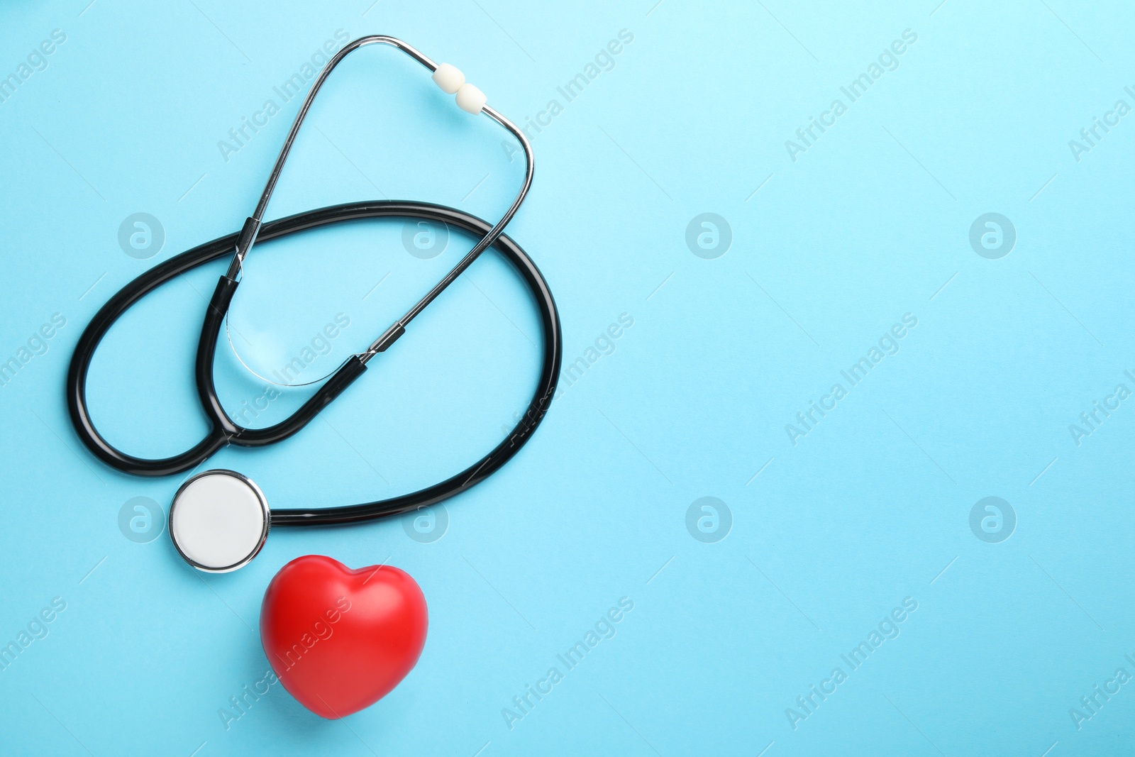 Photo of Stethoscope and red heart on light blue background, top view. Space for text