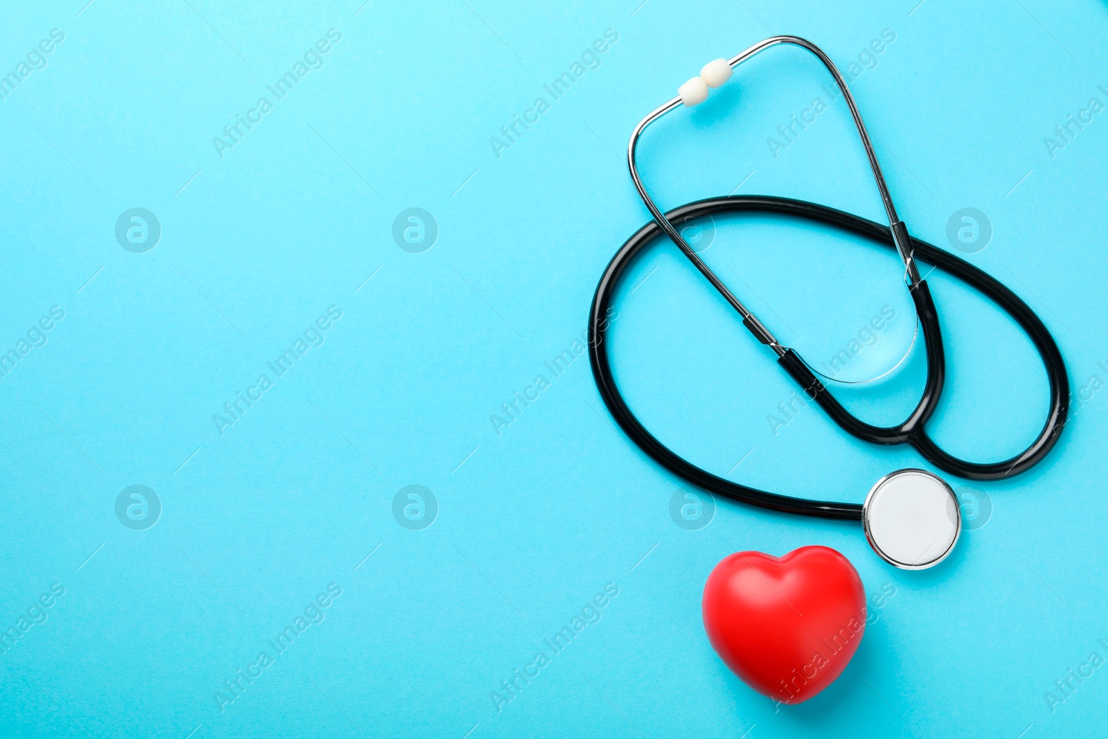 Photo of Stethoscope and red heart on light blue background, top view. Space for text