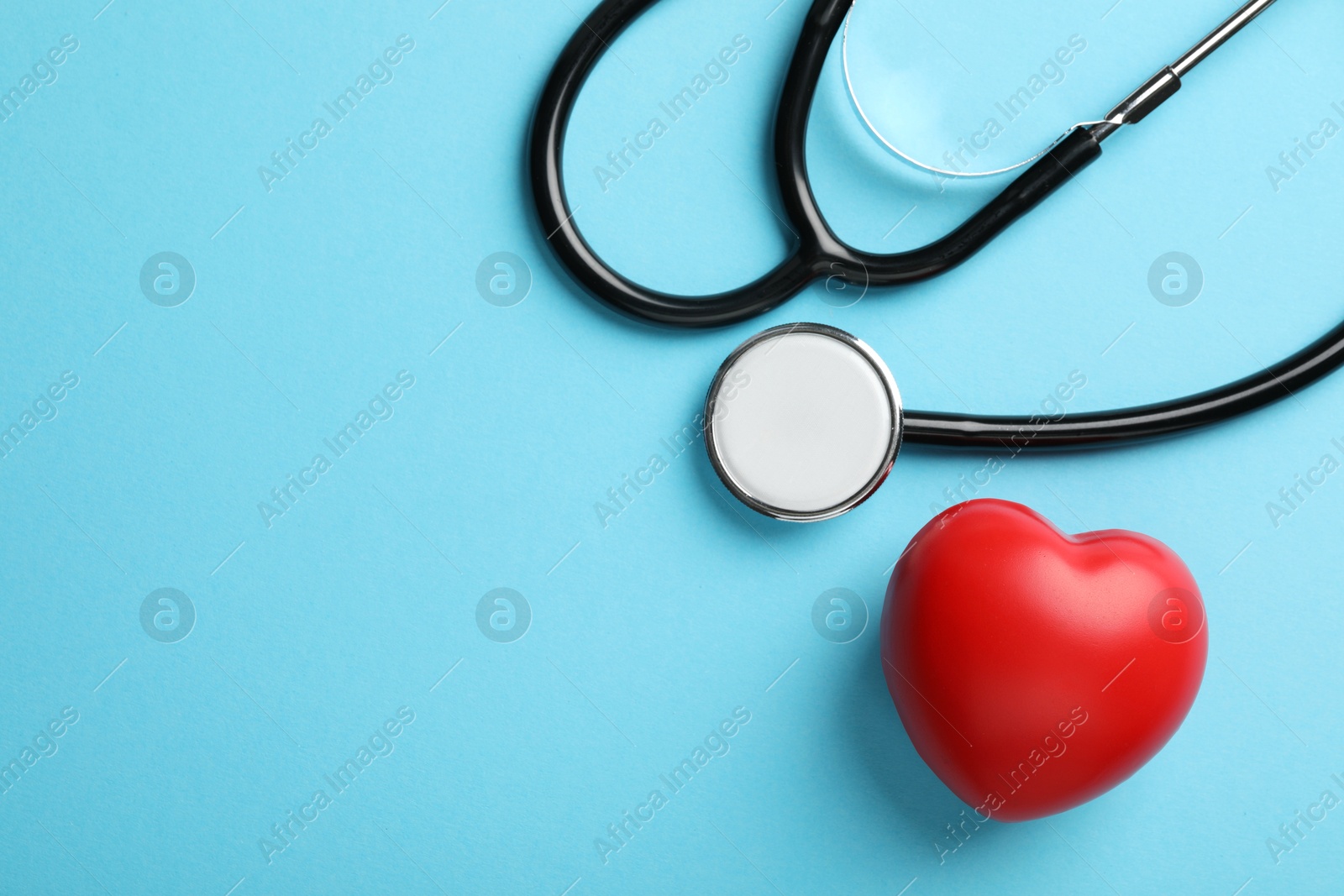 Photo of Stethoscope and red heart on light blue background, top view. Space for text