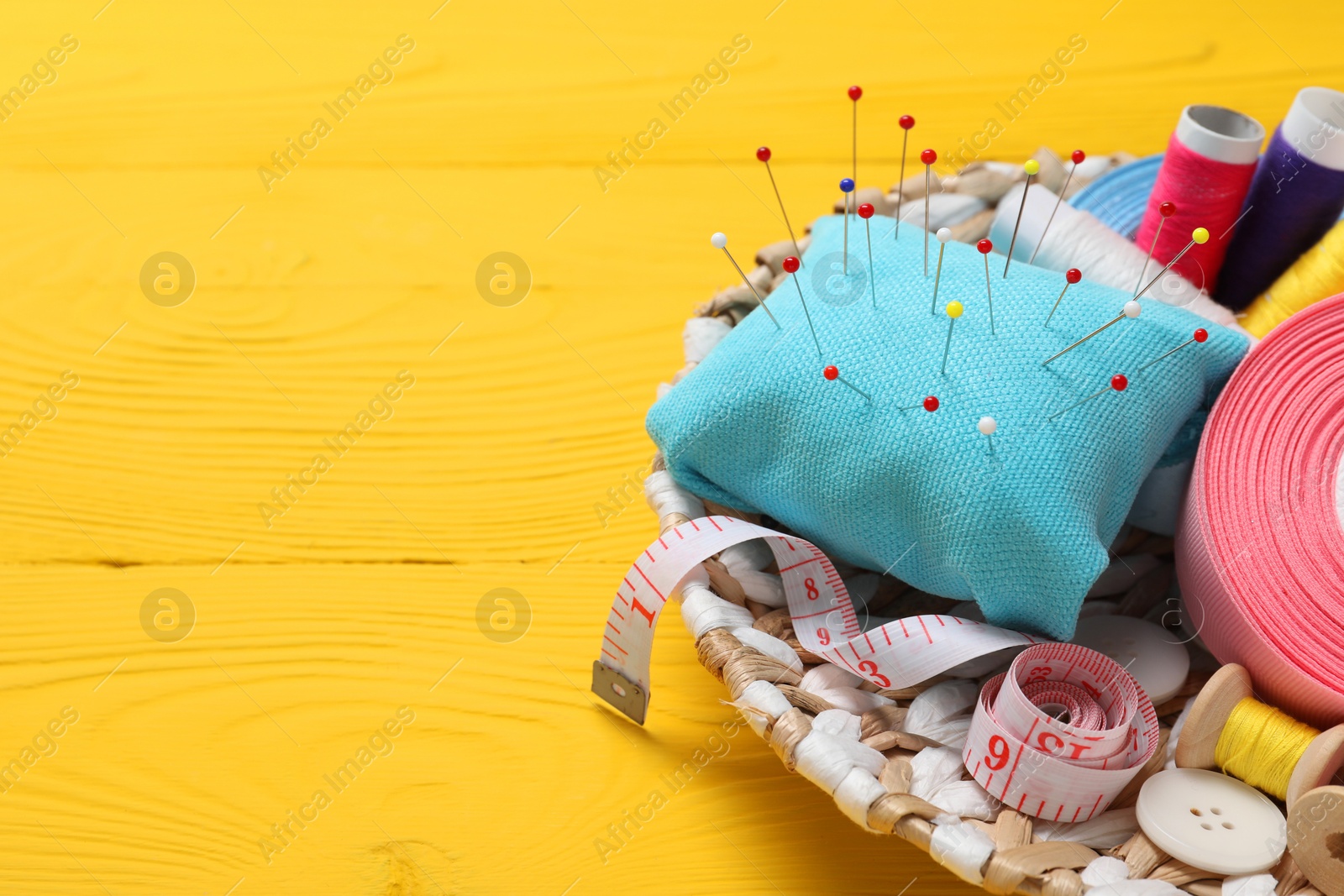 Photo of Light blue pincushion, pins and other sewing tools on yellow wooden table. Space for text