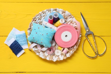 Light blue pincushion, pins and other sewing tools on yellow wooden table, flat lay