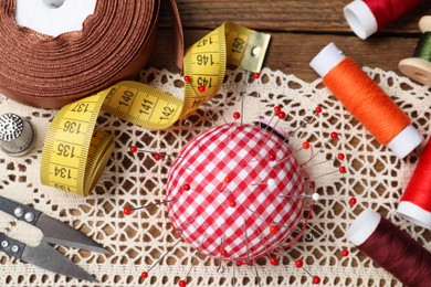 Photo of Checkered pincushion with pins and other sewing tools on wooden table, flat lay