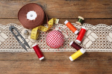 Checkered pincushion with pins and other sewing tools on wooden table, flat lay