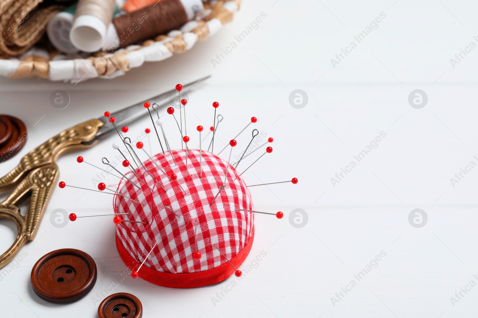 Photo of Checkered pincushion with pins and other sewing tools on white wooden table. Space for text