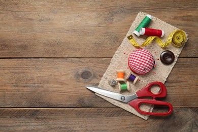 Checkered pincushion with pins and other sewing tools on wooden table, flat lay. Space for text