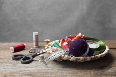 Blue pincushion with pins and other sewing tools on wooden table