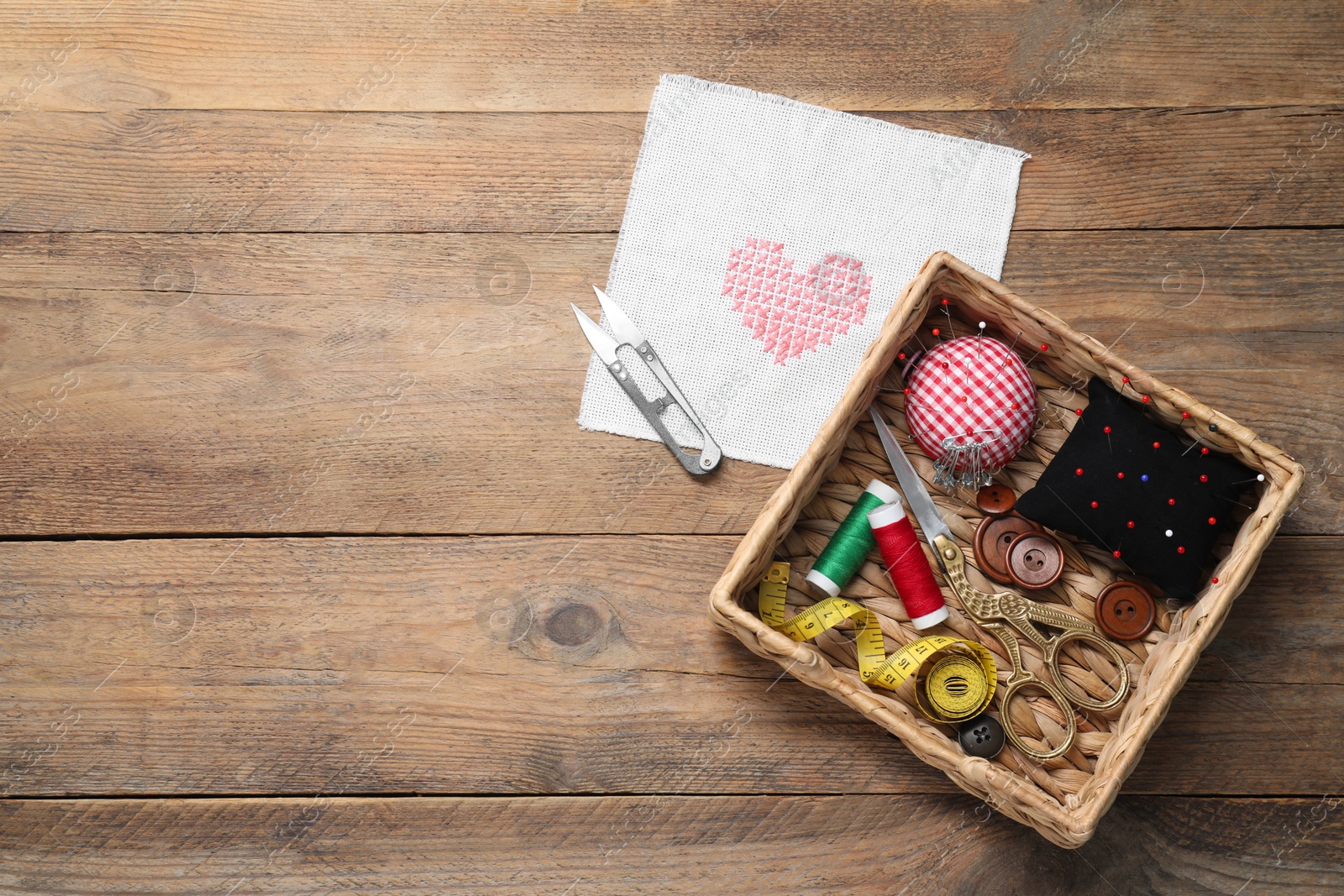 Photo of Pincushions with pins and other sewing tools on wooden table, flat lay. Space for text