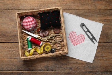 Pincushions with pins and other sewing tools on wooden table, flat lay