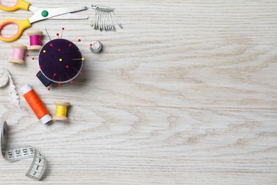 Photo of Blue pincushion with pins and other sewing tools on light wooden table, flat lay. Space for text