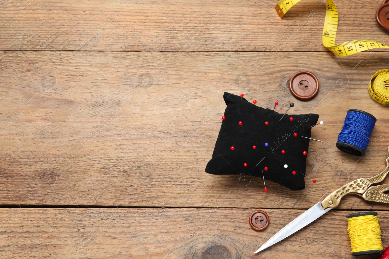 Photo of Blue pincushion with pins and other sewing tools on wooden table, flat lay. Space for text