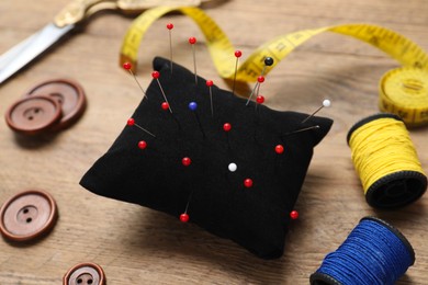 Blue pincushion with pins and other sewing tools on wooden table, closeup