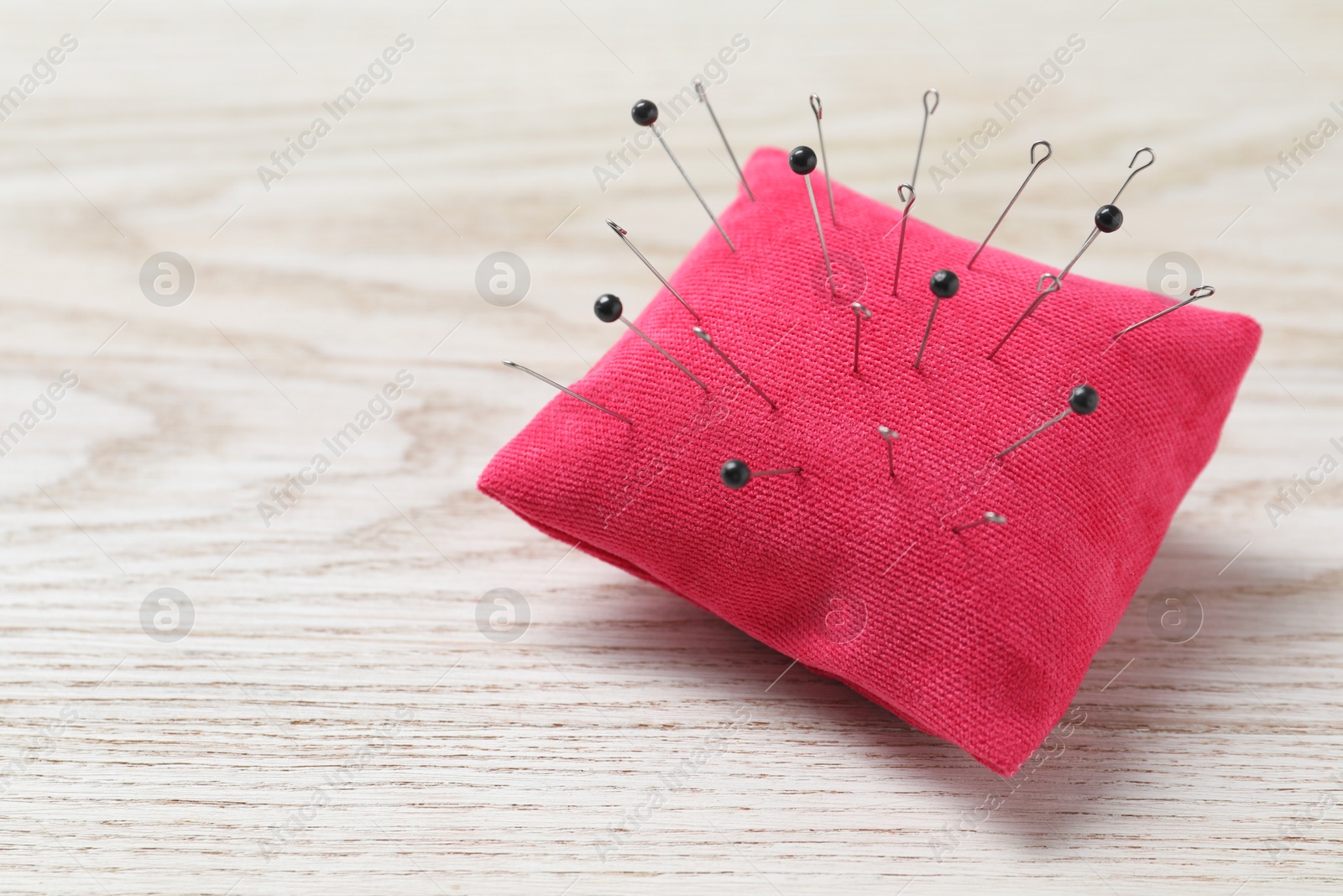 Photo of Red pincushion with sewing pins on light wooden table, closeup. Space for text