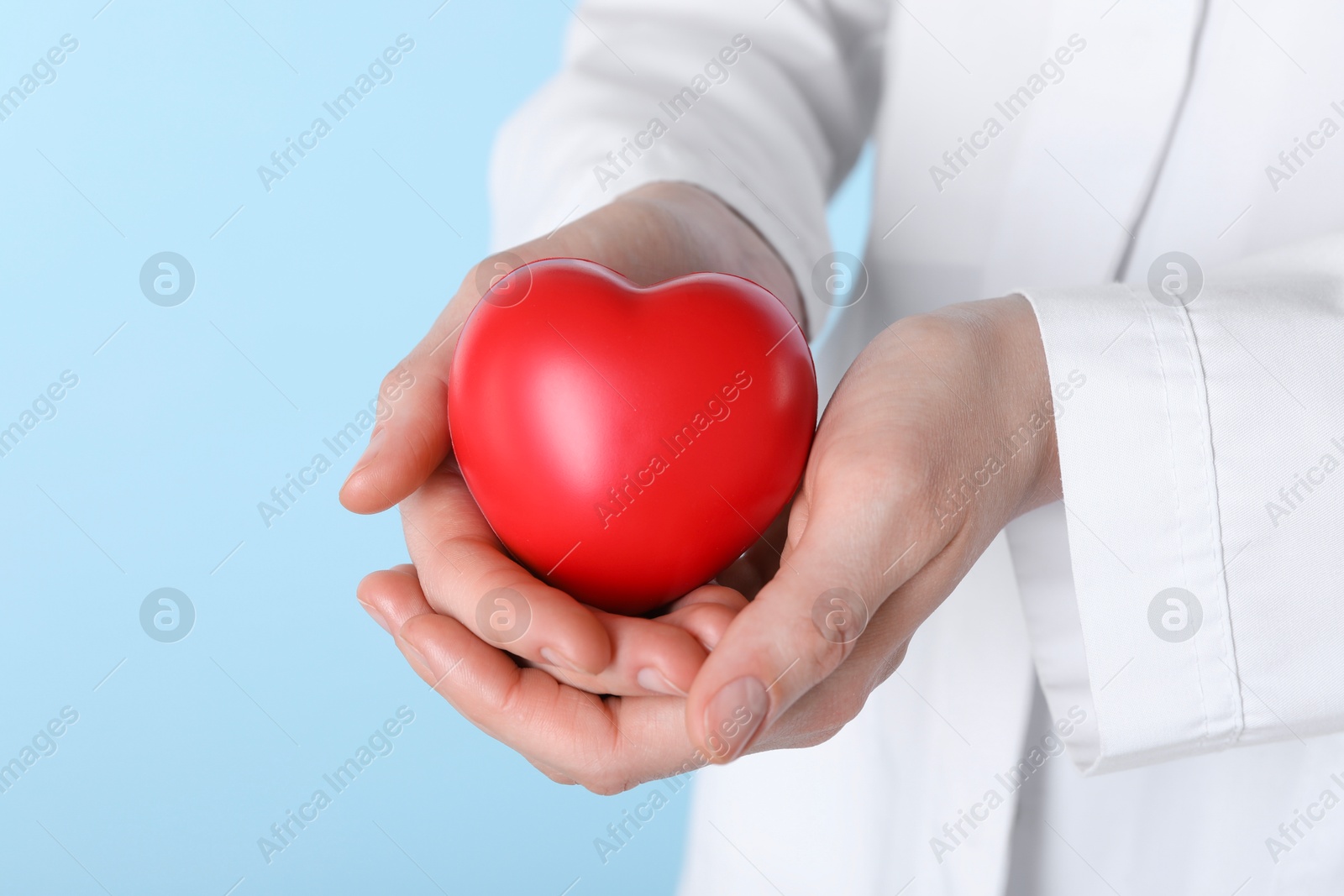 Photo of Doctor with red heart on light blue background, closeup