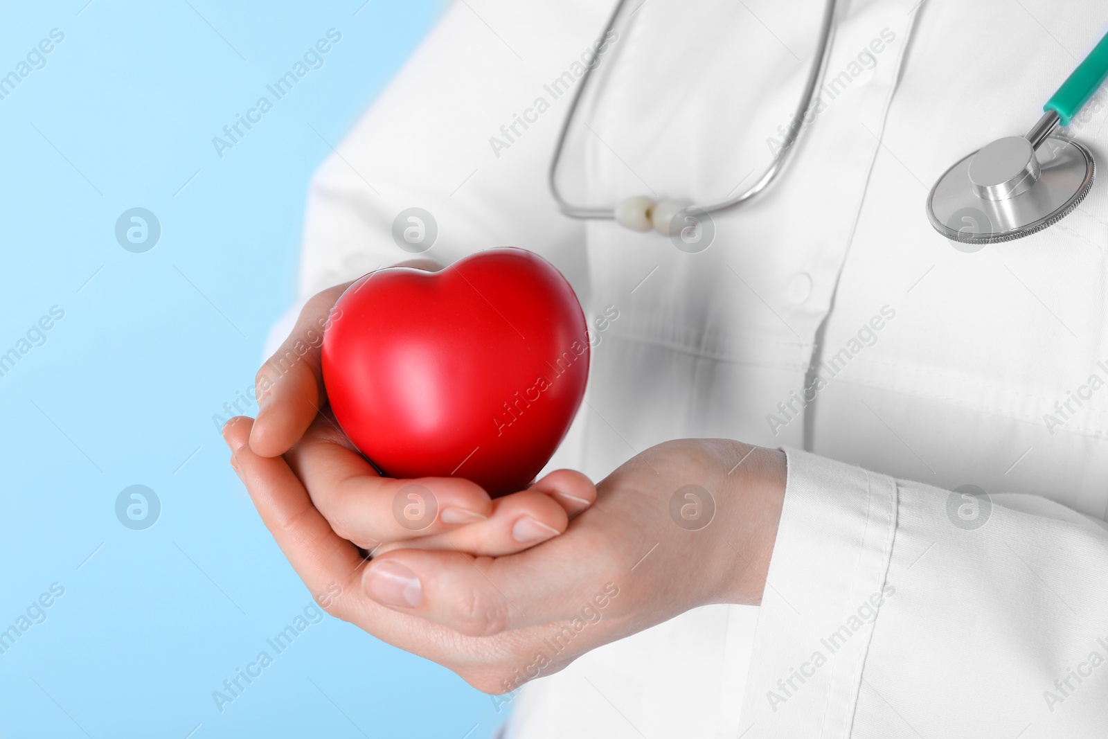 Photo of Doctor with red heart on light blue background, closeup