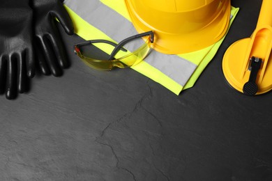 Photo of Yellow hard hat and other personal protective equipment on black surface, flat lay. Space for text