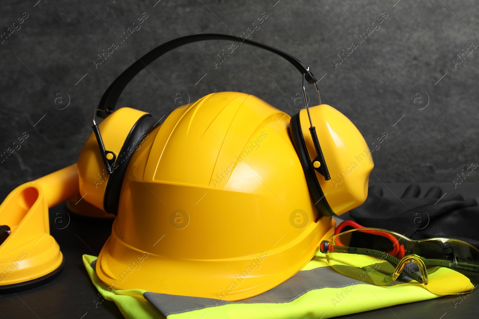 Photo of Yellow hard hat, earmuffs and other personal protective equipment on black surface, closeup