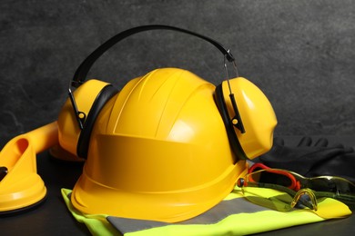 Photo of Yellow hard hat, earmuffs and other personal protective equipment on black surface, closeup