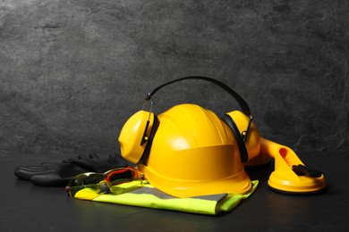 Yellow hard hat, earmuffs and other personal protective equipment on black surface