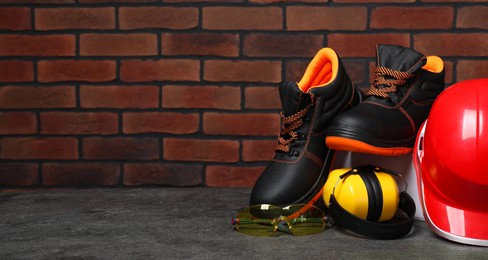 Photo of Pair of working boots, hard hat, protective goggles and earmuffs on grey surface. Space for text