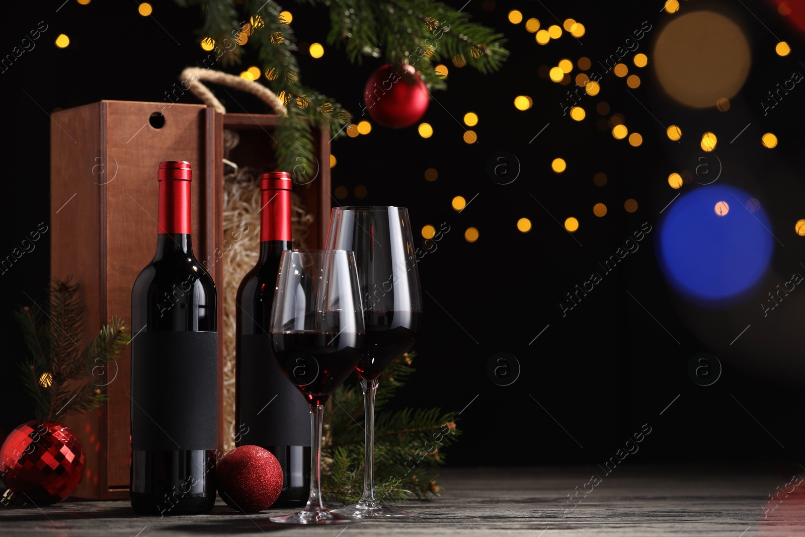 Photo of Bottles of wine, glasses, wooden boxes, fir twigs and red Christmas balls on table, space for text