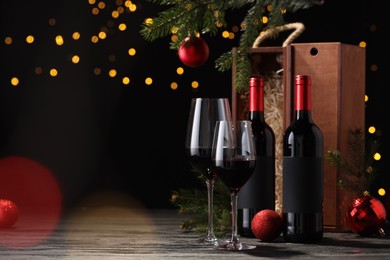 Photo of Bottles of wine, glasses, wooden boxes, fir twigs and red Christmas balls on table, space for text
