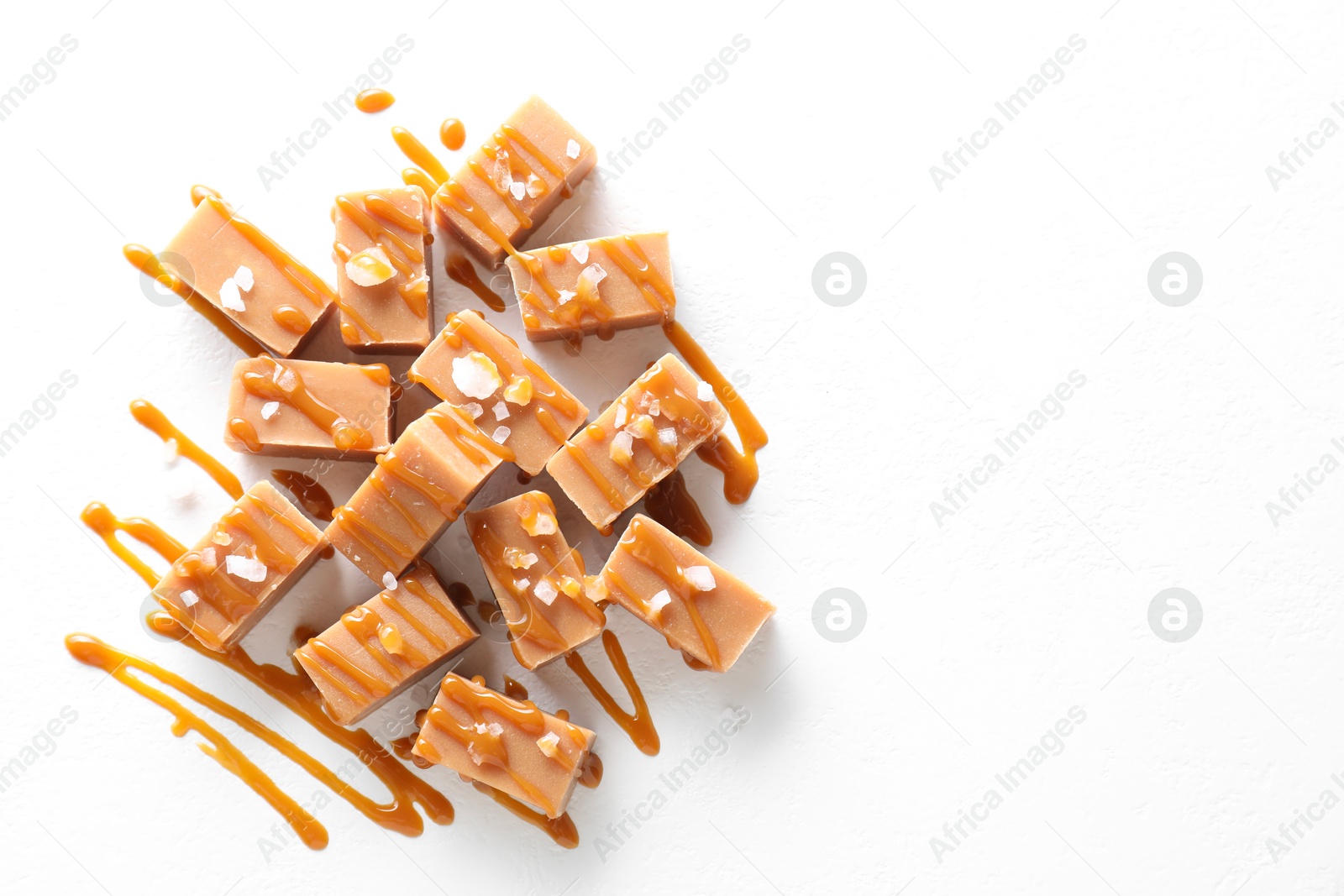 Photo of Tasty candies, caramel sauce and salt on white table, top view. Space for text