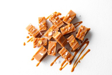 Photo of Tasty candies, caramel sauce and salt on white table, top view