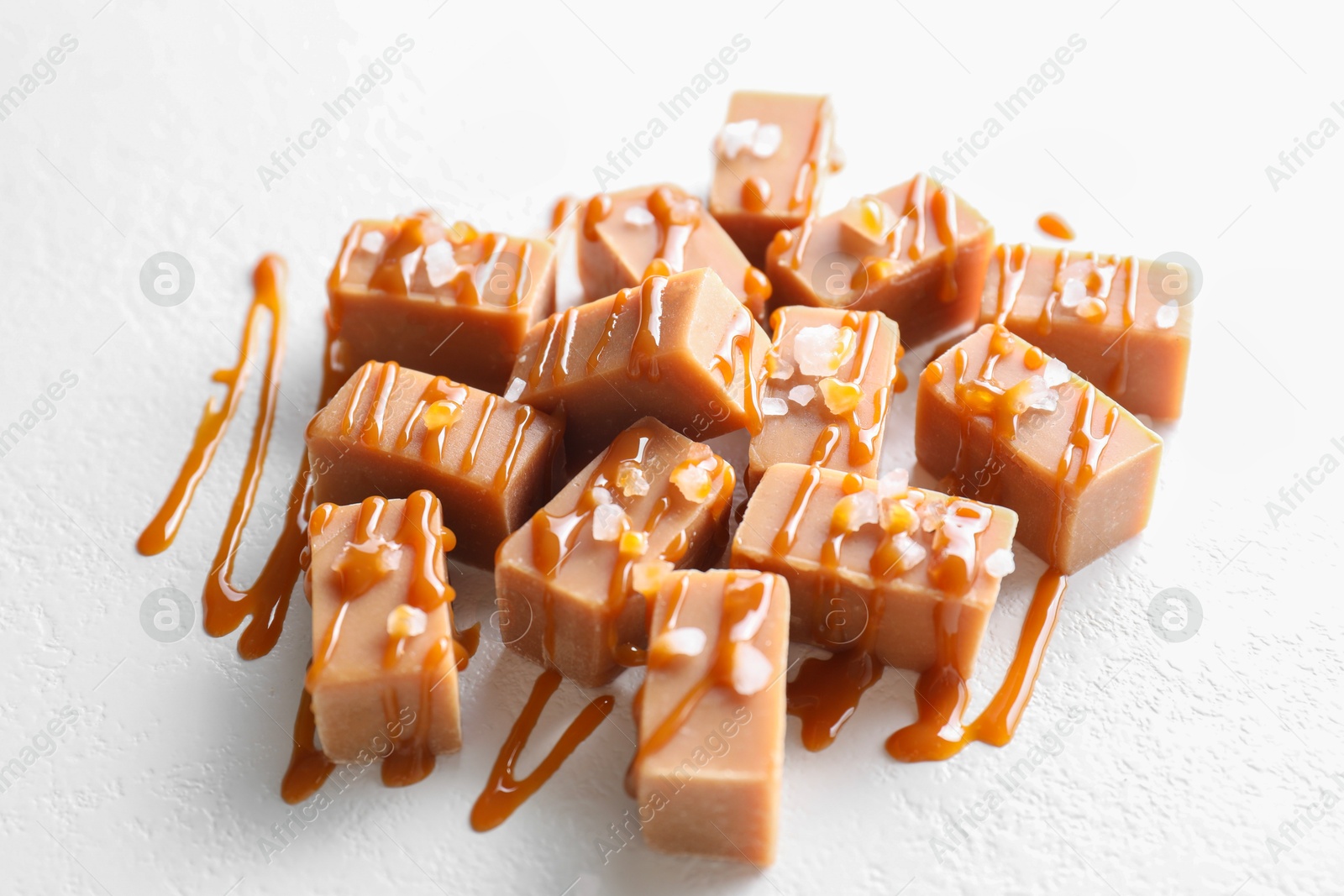 Photo of Tasty candies, caramel sauce and salt on white table