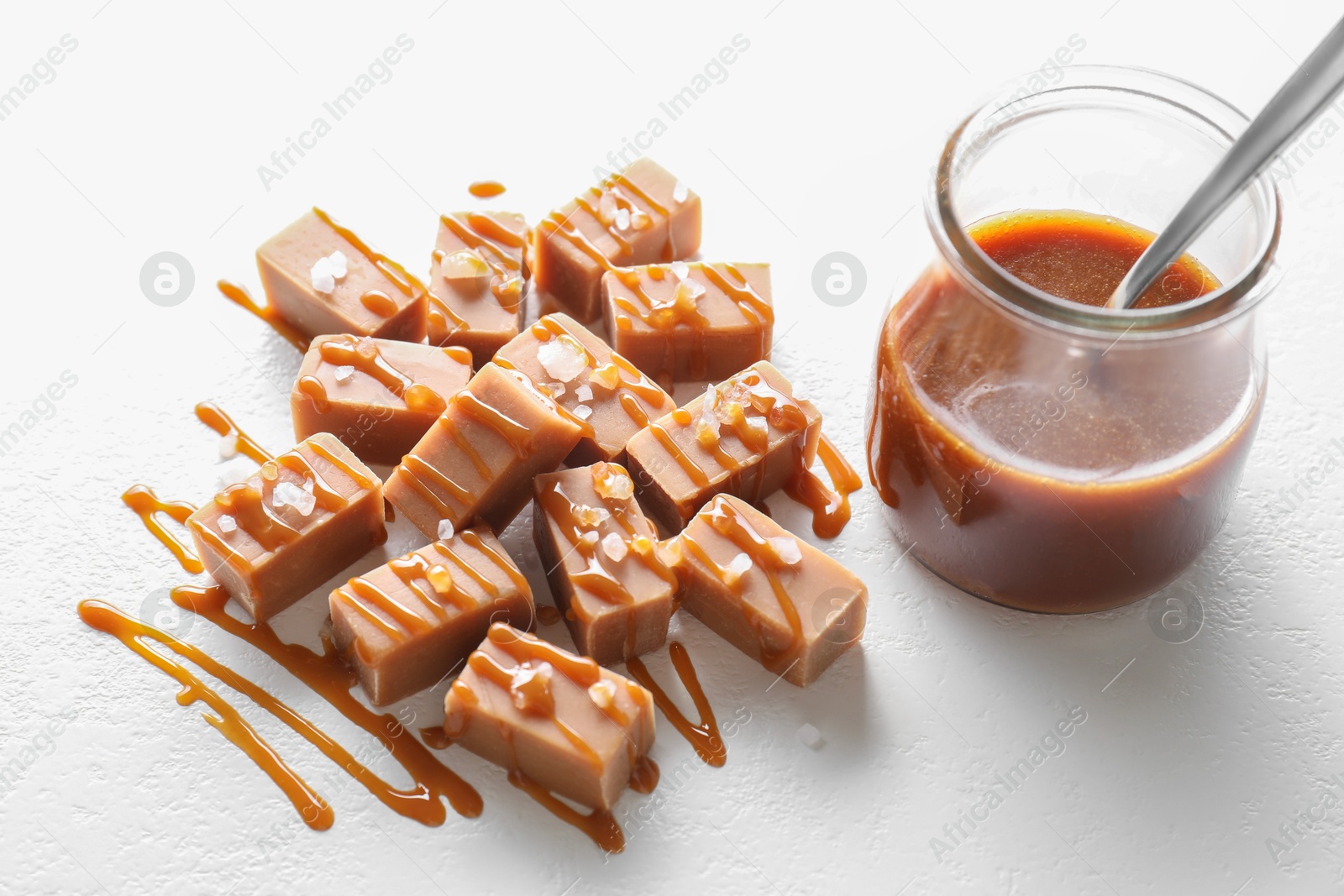 Photo of Tasty candies, caramel sauce and salt on white table