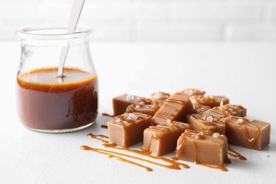 Photo of Tasty candies, caramel sauce and salt on white table