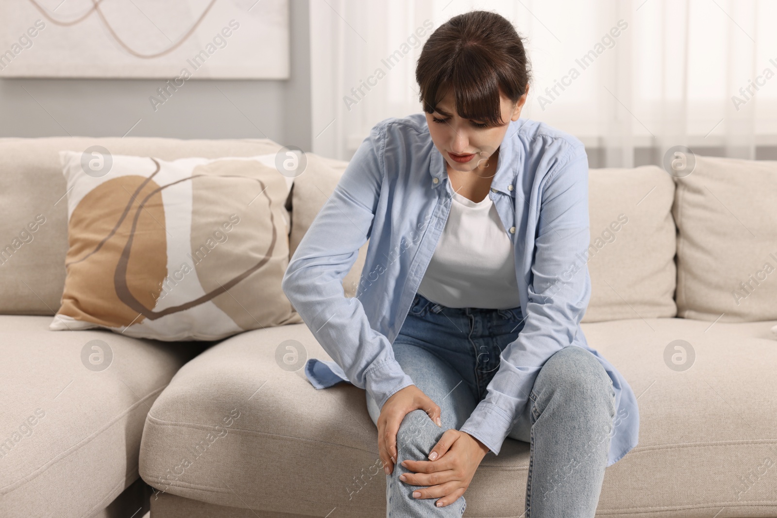 Photo of Upset woman suffering from knee pain on sofa at home