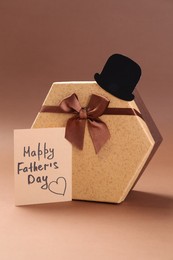 Photo of Card with phrase Happy Father's Day, hat and gift box on light brown background