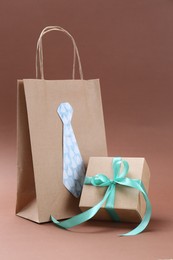 Photo of Happy Father's Day. Paper bag with tie and gift box on light brown background