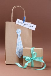 Photo of Happy Father's Day. Paper bag with tie, phrase Love You Dad and gift box on light brown background