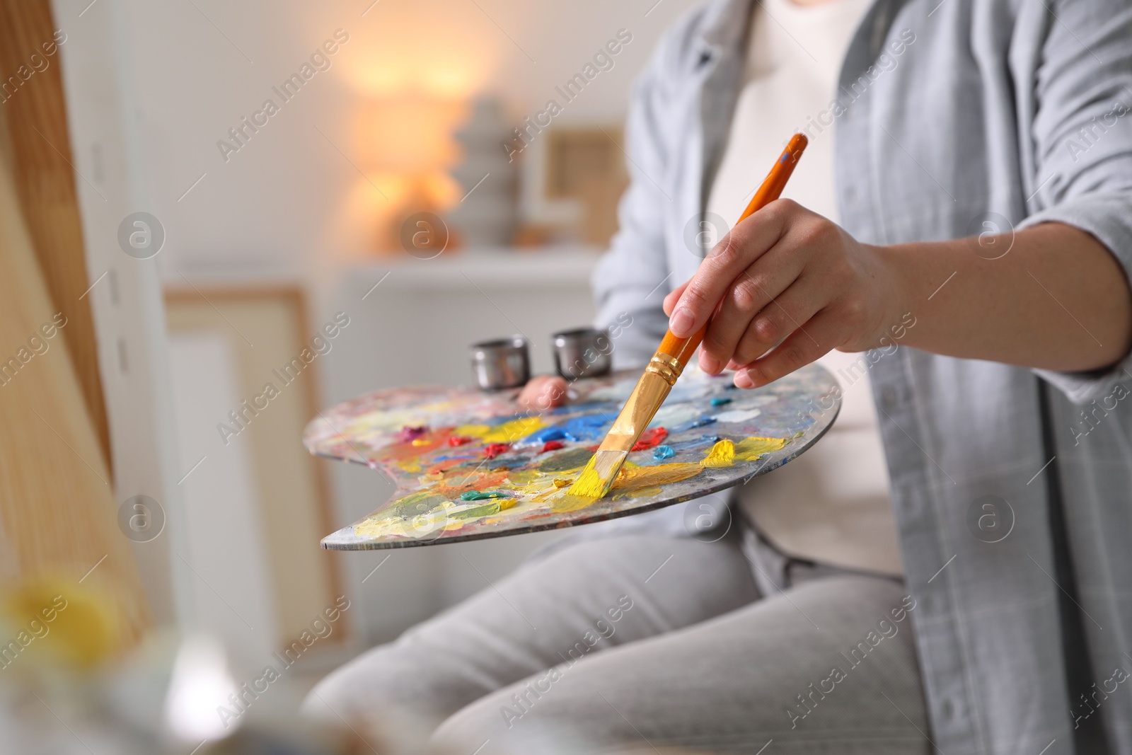 Photo of Woman with brush using palette near easel indoors, closeup