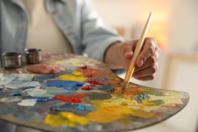 Photo of Woman mixing paints on palette with brush indoors, closeup