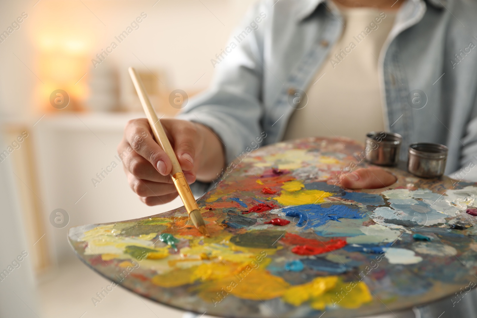 Photo of Woman mixing paints on palette with brush indoors, closeup