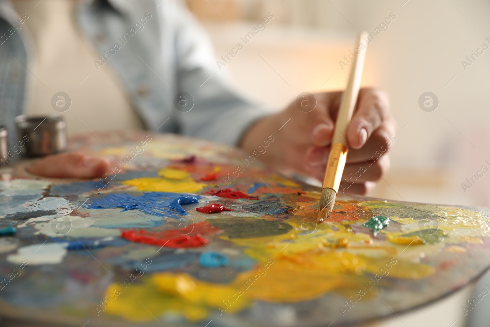 Photo of Woman mixing paints on palette with brush indoors, closeup