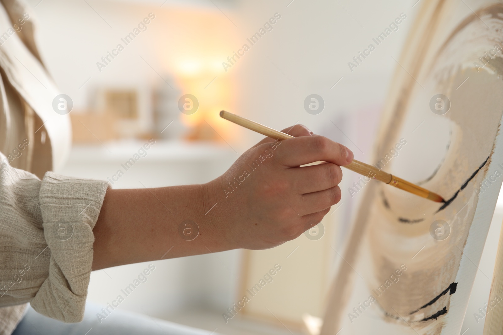 Photo of Woman painting on easel with canvas indoors, closeup