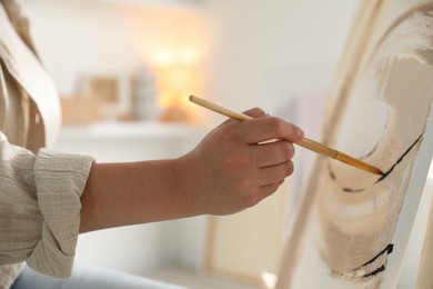 Photo of Woman painting on easel with canvas indoors, closeup