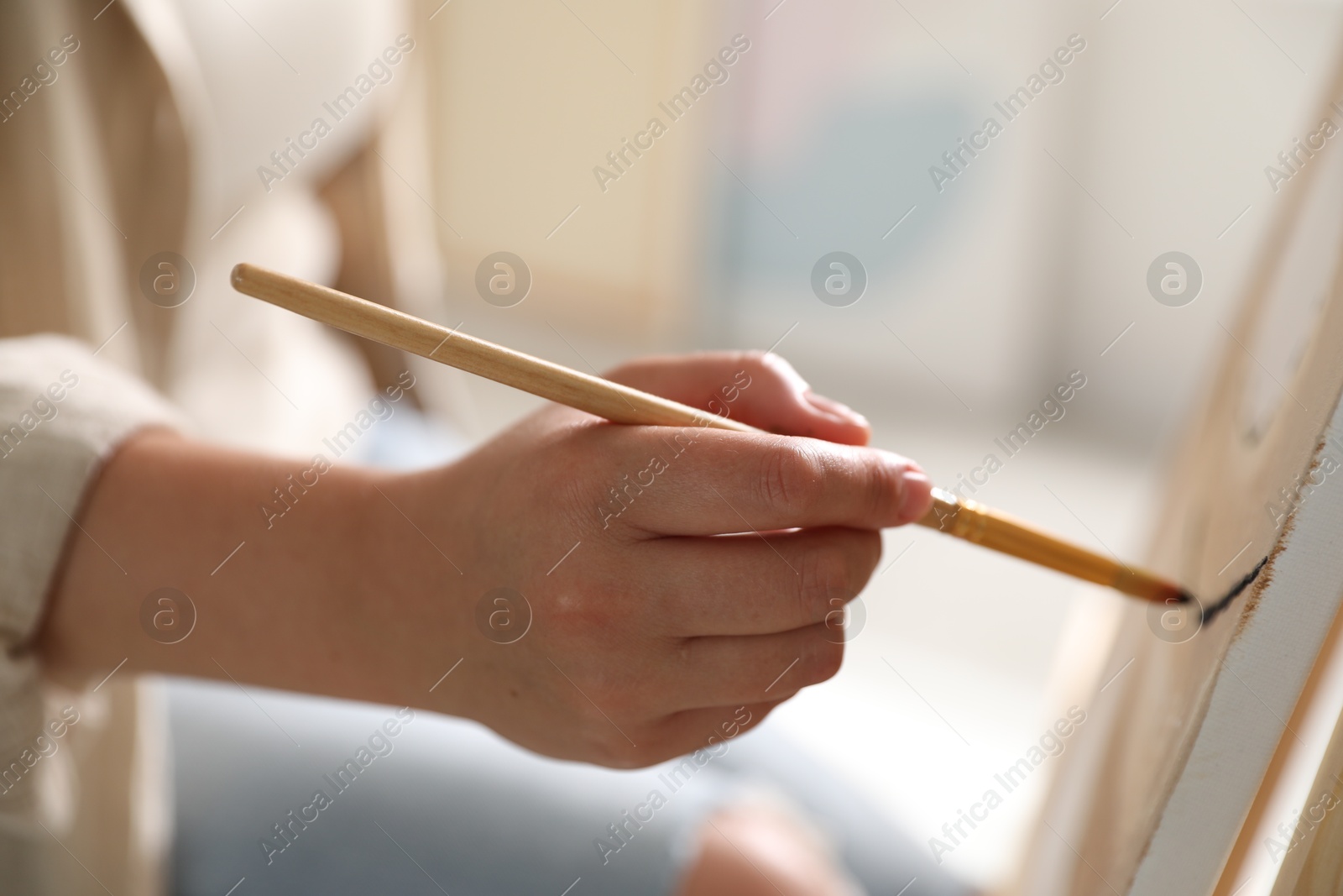 Photo of Woman painting on easel with canvas indoors, closeup