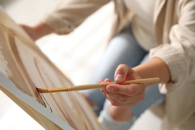 Photo of Woman painting on easel with canvas indoors, closeup