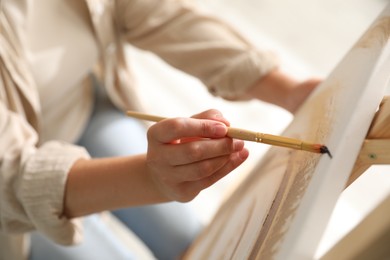 Photo of Woman painting on easel with canvas indoors, closeup