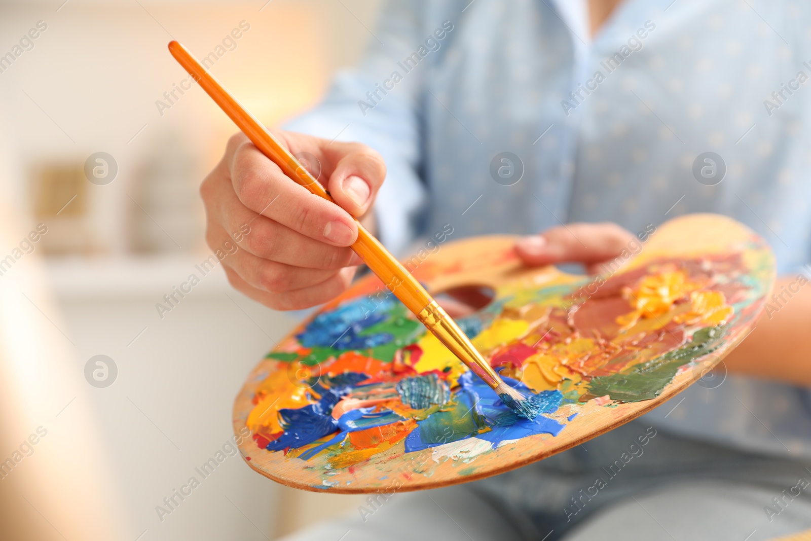 Photo of Woman mixing paints on palette with brush indoors, closeup