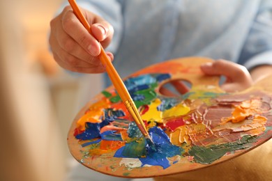Photo of Woman mixing paints on palette with brush indoors, closeup