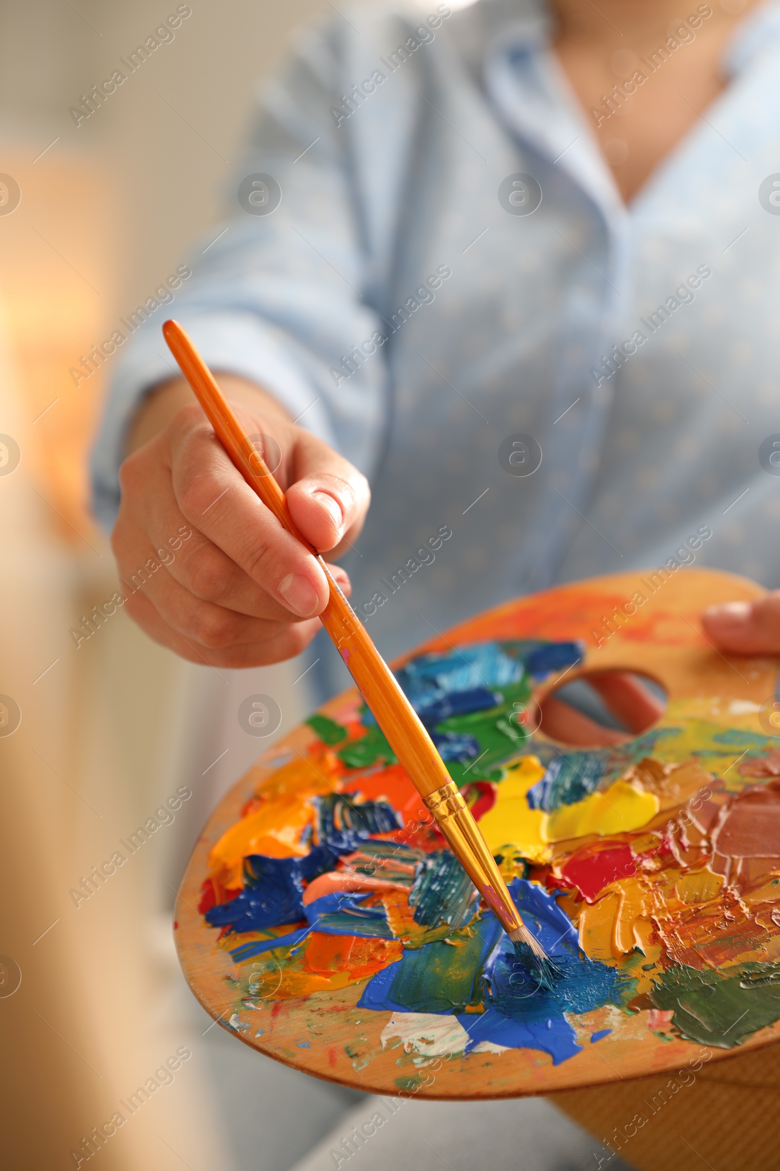 Photo of Woman mixing paints on palette with brush indoors, closeup