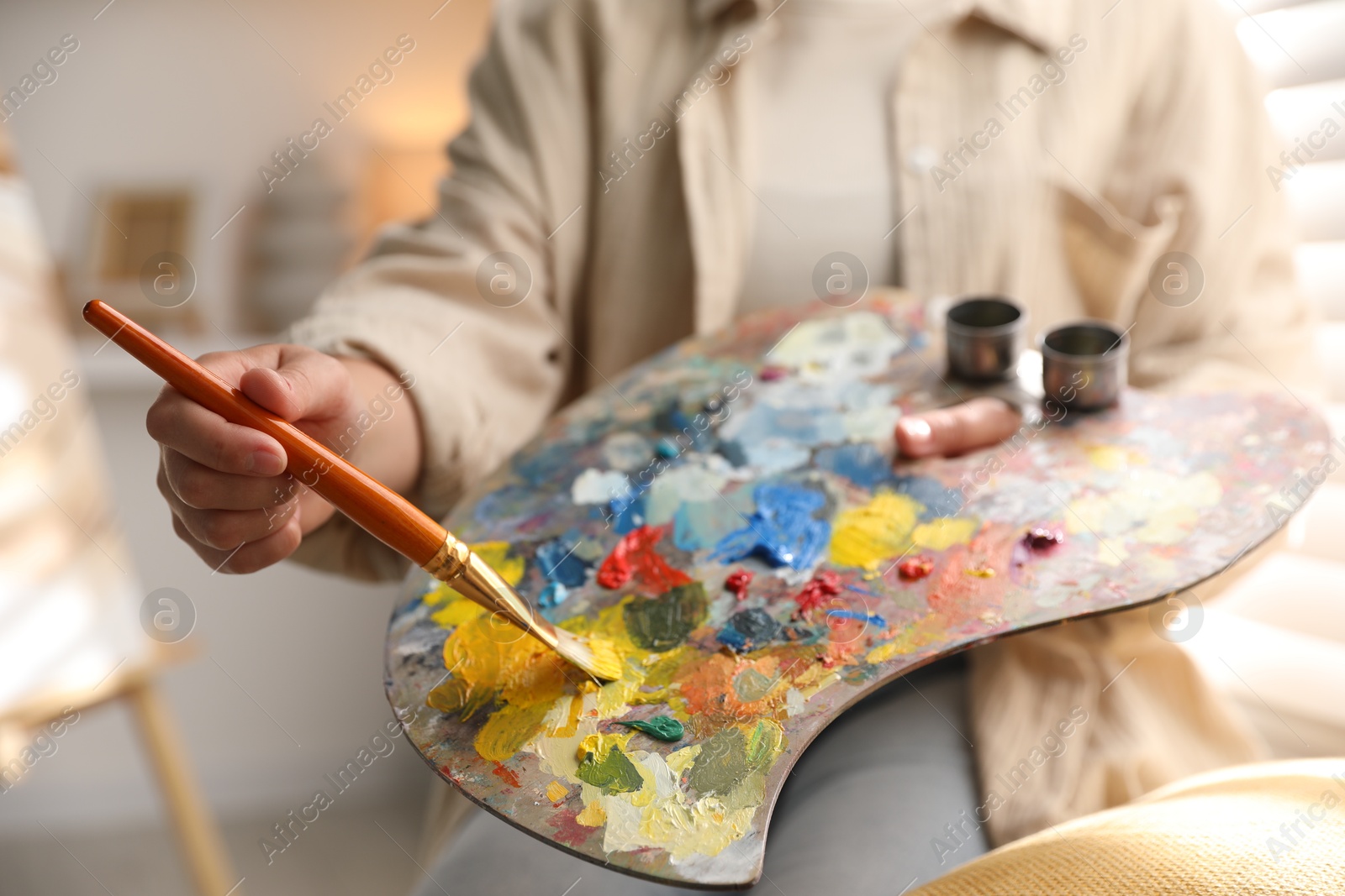 Photo of Woman mixing paints on palette with brush indoors, closeup